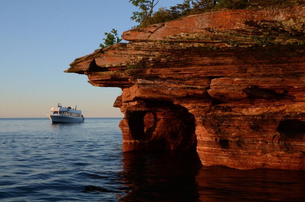 An Apostle Island cruise can be seen in the distance, passing by the craggy cliffs of Devils Island.