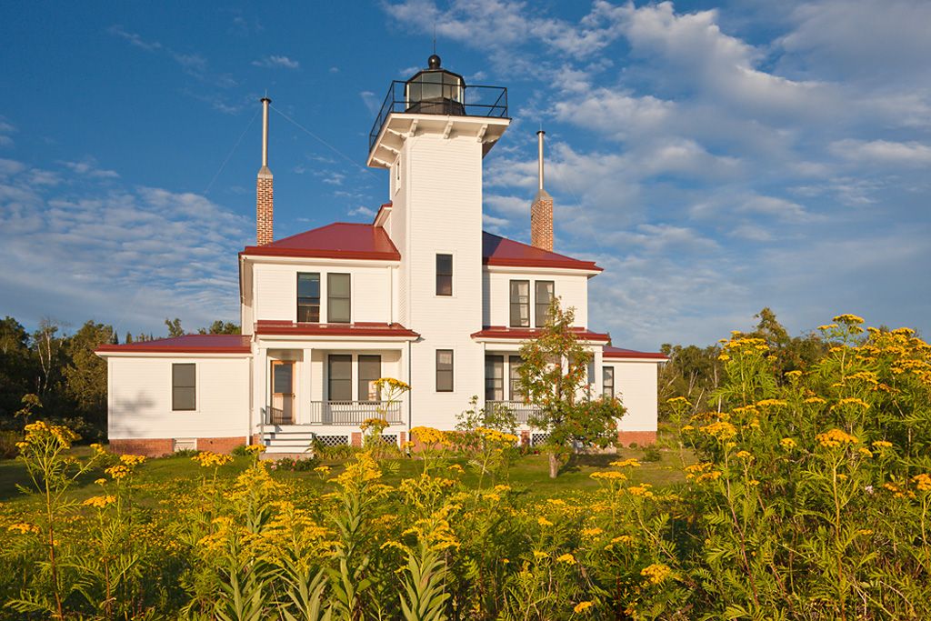 The Raspberry Island Lighthouse is white with red roofing. It is three levels, with a tower in its center.