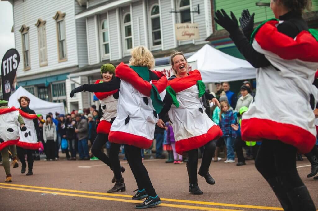 People dressed as apple cores dancing in the street for a festival.