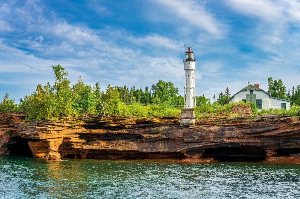 Rocky cliff shore with trees and a lighthouse and blue sky.