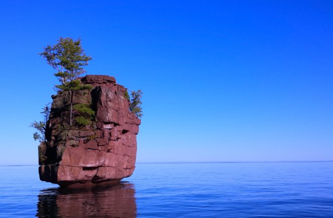 Lone rock outcropping in the middle of a lake with not shore in sight.