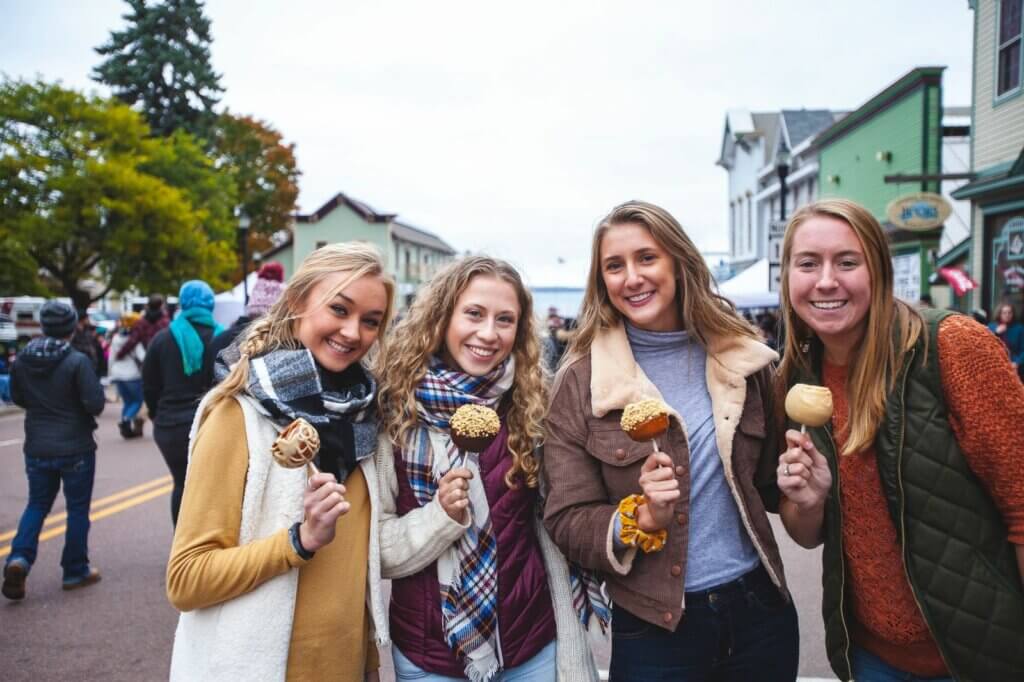 Four Caucasian women holding candied apples in a town square.