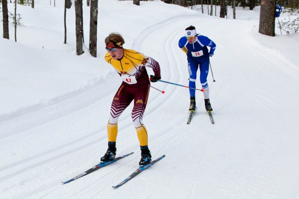 Two men skiing along a trail in the middle of the forest.