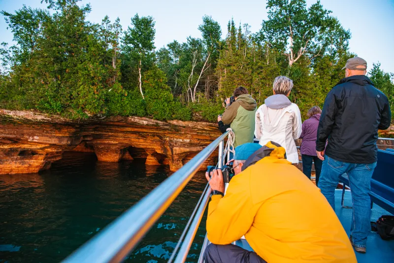 A man crouching on the top deck of an Apostle Islands Cruise with a camera to get a great shot of Devils Island.