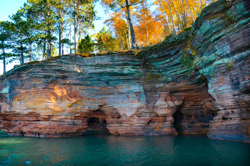 Trees with autumn colors top the multi-colored cliffs of Devils Island